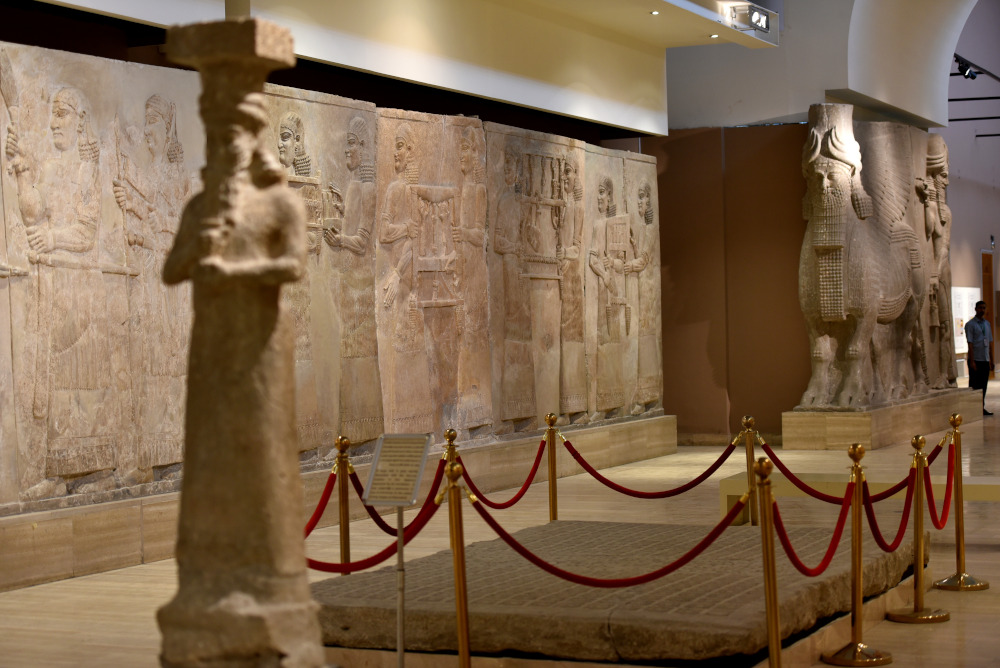 Room X, the Grand Assyrian Gallery at the Iraq Museum in Baghdad. The gypsum wall reliefs are part of a long tributary scene; Sargon II receives tribute from Urartu (modern-day Armenia). The reliefs as well as the lamassu and the statue of the god Ea (in the foreground; blurred) came from Khorsabad, Iraq. Circa 710 BCE. Photo courtesy of the author.