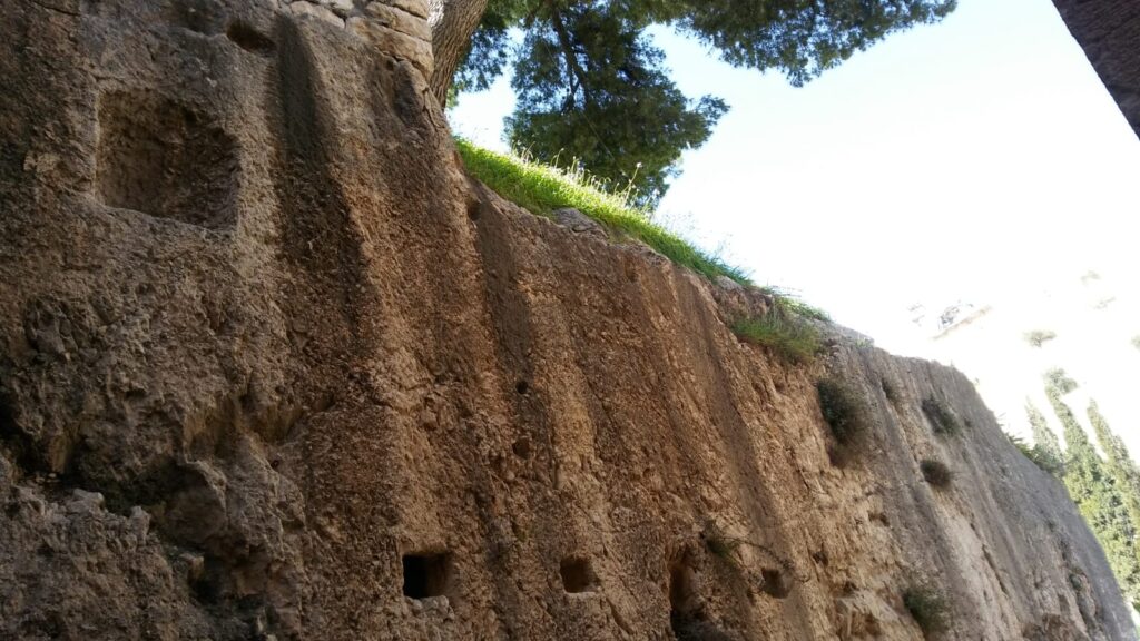 Northern face of the bedrock opposite the entrance to the tomb, showing three square slots hewn into the bedrock for entrance to the tomb along with a later enclosure that presumably held a relic/statue. (Photo by Joe Zias)