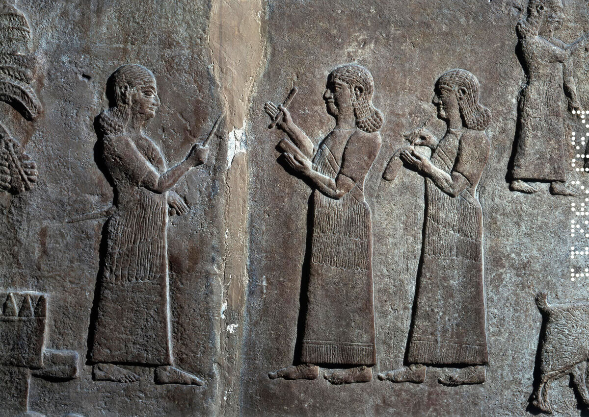 Detail of an alabaster wall panel relief showing two scribes. The first holds a clay-tablet in his left hand; the second is writing on a roll presumably made of leather. Nimrud: Central Palace, 8th century BCE. Museum number: BM 1848,1104.5. © The Trustees of the British Museum