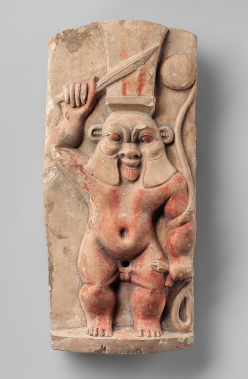 Bes appears frontally, waving a knife in one hand and in the other grasps a snake. The snake holds a rounded object, most likely a tambourine.