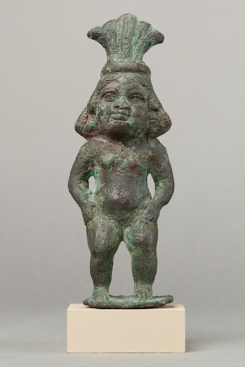 A nude standing Beset with long hair wearing a feathered headdress.