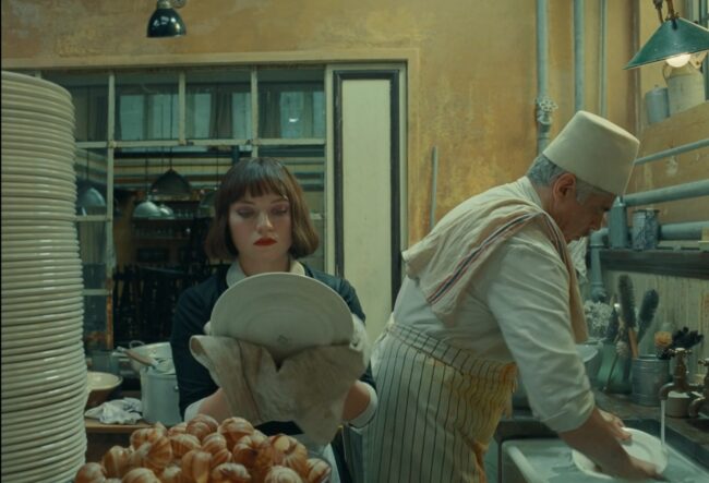 At the end of the film, Korda abandons his grand "Phoenician Scheme" in favor of running a humble bohemian French café alongside his daughter Liesel. He still wears the white Fez. Still image from The Phoenician Scheme (2025), directed by Wes Anderson. Courtesy of Focus Features.